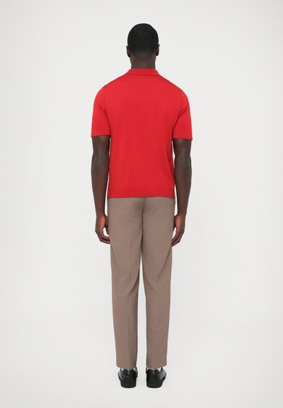 Punainen lyhythihainen poolopaita yhdistettynä ruskeisiin housuihin ja mustiin kenkiin. Poolopaidassa on ribbineulosta ja klassinen kaulassuunnittelu.