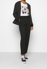 Veste bombardier noire matelassée, t-shirt blanc avec un graphique de palmier et un texte rouge, pantalon noir taille haute, baskets noir et blanc avec des accents roses.