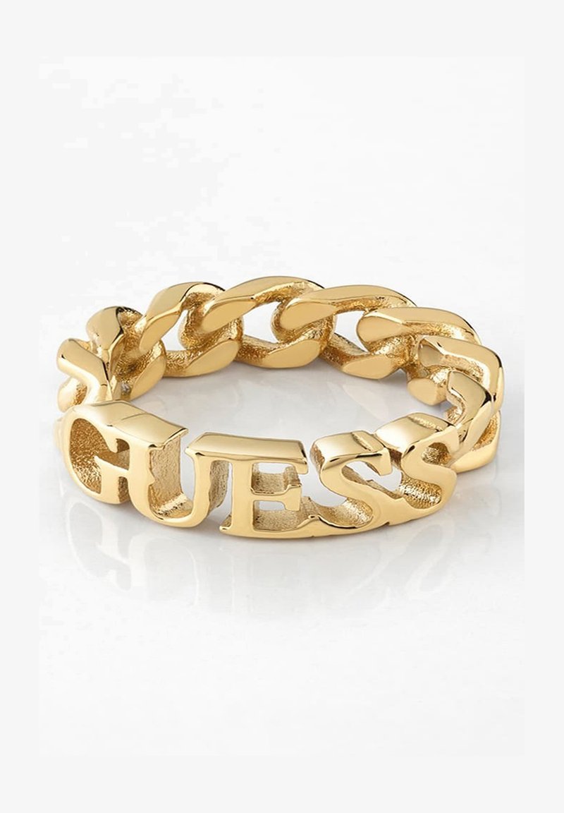 Gold ring featuring a linked chain design with the word "GUESS" shaped prominently in block letters, smooth textured surface.