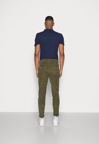 Mörk marinblå polo skjorta, olivgröna kordflorsbyxor och vita sneakers. Fokusera på modern design och texturerat tyg. Baksidan.