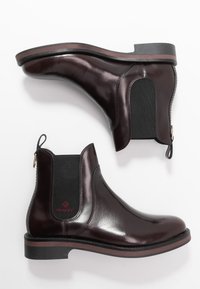 Botas Chelsea de cuero marrón oscuro con paneles elásticos laterales negros, lengüetas y suelas rayadas, colocadas una al lado de la otra sobre un fondo blanco.