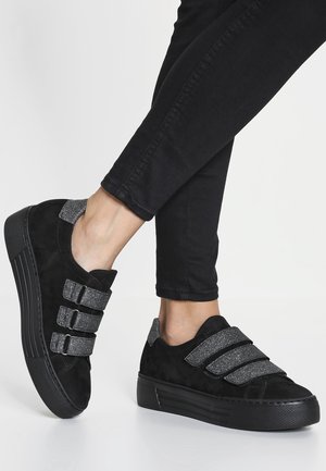 Sorte platform-sneakers med tre brede glitrende grå remme og matchende hældetalje båret med sorte smalle bukser.