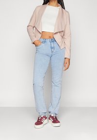 Ljusrosa, öppen jacka över en vit crop top, tillsammans med ljusblå raka jeans och vinröda sneakers med vita detaljer.