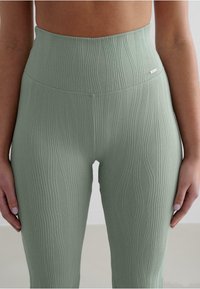 High-waisted leggings in light green ribbed fabric, featuring a textured wave pattern and a small logo accent on the waist.