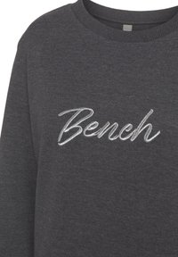 Grauer Sweatshirt mit Rundhalsausschnitt und einem dekorativen, silbernen, bestickten "Bench"-Logo auf der Vorderseite. Das Material wirkt weich und strukturiert.