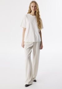 Weißes Baumwoll-T-Shirt mit kurzen Ärmeln, kombiniert mit beigen Cargo-Hosen, die seitliche Taschen und einen lässigen Schnitt aufweisen; schwarze spitze Schuhe.