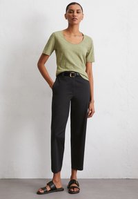 T-shirt verde oliva a maniche corte, pantaloni neri a vita alta e sandali neri con un accento dorato. Texture morbide, vestibilità rilassata.