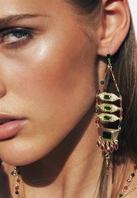 Boucles d'oreilles en or arborant un design complexe avec des pierres précieuses vertes et violettes, présentant une forme en cascade et de nombreux accents détaillés.