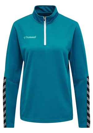 Teal langærmet træningstrøje med halvdels-zipkrave, tekstureret stof og sort-hvide chevronmønstrede detaljer på ærmerne.