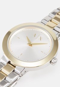 Orologio con finitura argento e oro, con cassa rotonda, quadrante argentato spazzolato, lancette dorate, tre indicatori a diamante e bracciale metallico a maglie.