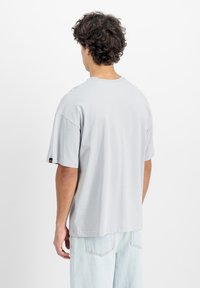 Svijetlosivi pamučni majica s kratkim rukavima, blago prevelikog kroja, rebrasta izreza i oznaka na lijevom rukavu.