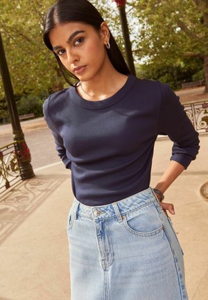 Marineblaues, geripptes Langarmshirt kombiniert mit einem hoch taillierten, hellblauen Denimrock, der Taschen und einen leichten Used-Look aufweist.