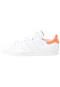 White leather sneaker with orange heel accent, perforated sides, lace-up design, and rubber outsole. Features adidas logo on the tongue and side.