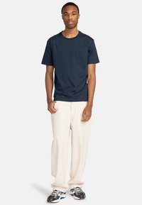 Navy katoenen t-shirt met een ronde hals en een borstzak, gecombineerd met losse crèmekleurige broeken en geblokte sportschoenen.