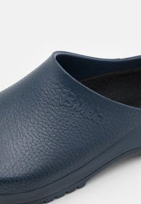 Sabot bleumarin realizat dintr-un material texturat, cu un logo reliefat. Design cu vârf rotunjit și spate deschis, având o talpă striată pentru aderență.