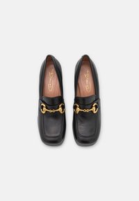 Sorte læderloafers med firkantet tå, med en guldkædeaccent over overdelen og en glat tekstur. Indersiden har et lyst brunt foer.