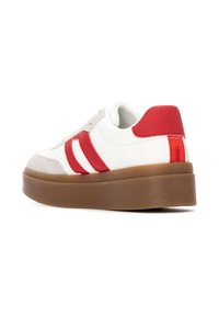 Zapatilla blanca con rayas y acentos rojos, con una puntera de ante gris y una suela de plataforma marrón. Textura suave con diseño de cordones.