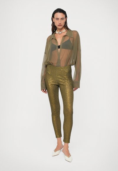 Priehľadná olivovo zelená blúzka, pod ňou čierny top, doplnená priliehavými zlatými flitrovými legínami. Biele mule topánky dokončujú vzhľad a pridávajú kontrast.
