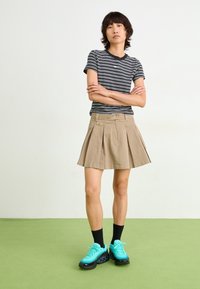 Raidallinen mustavalkoinen T-paita, khakivärinen laskostettu hame, mustat nilkkasukat ja kirkkaan teal-väriset tennarit mustilla yksityiskohdilla. Yksinkertainen muotoilu, rento istuvuus.