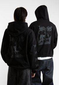 Felpa nera con cappuccio e stampa grafica sulla schiena che presenta la silhouette di una casa. Realizzata in materiale morbido con una vestibilità comoda.