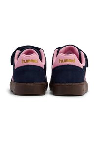 Granatowe zamszowe tenisówki z różowymi tkaninowymi akcentami, wyściełanym kołnierzem i paskiem na rzep. Brązowa gumowa podeszwa z logo z tyłu.