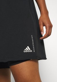 Camiseta negra de mangas cortas, hecha de suave algodón, con un logo blanco de Adidas y un texto que dice "El algodón reciclado ahorra agua."