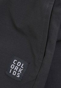 Schwarzer Stoff mit gerippter Textur, der ein quadratisches Patch mit der Aufschrift "COLOR KIDS" in Weiß zeigt. Das Design ist einfach und funktional.