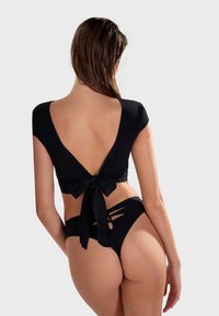 Crni bikini set koji se sastoji od kratkotrajnog topa s niskim leđima i vezanjem mašnom, uparen s visokim gaćicama s izrezima.