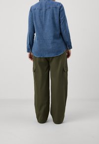 Denim shirt with long sleeves, rounded hem, and blue hue. Paired with olive cargo pants featuring side pockets and a relaxed fit.
