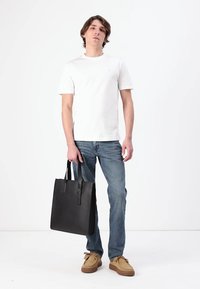 Bolso tote de cuero negro con dos asas, diseño simple. Llevado con una camiseta blanca, jeans azul claro y zapatos beige.