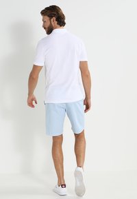 Polo shirt bianco, pantaloni corti azzurri e sneakers bianche. Il polo ha maniche corte, e i pantaloni corti sono casual con una vestibilità rilassata. Design semplice.
