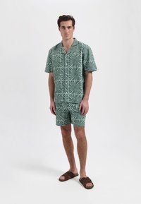 Korte mouwen groene shirt en bijpassende shorts met een wit loofpatroon, gemaakt van lichtgewicht stof. Bevat knopen en heeft een relaxed fit.