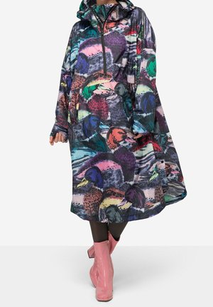 Femme portant un imperméable à capuche coloré avec des motifs abstraits de canards, associé à des collants noirs et des bottines roses.