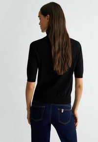 Top in maglia nera a maniche corte con design aderente. Tessuto testurizzato, polsini e orlo a coste. Abbinato a jeans in denim blu scuro.