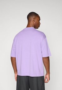 Purple short-sleeve t-shirt with a crew neck, relaxed fit, plain fabric, and visible stitching details, worn with black textured shorts.