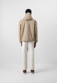 Beige waterproof jacket with a hood, straight hem, and subtle texture. Paired with white wide-leg pants and brown sneakers.