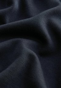 Marineblauwe stof met een gladde, zachte textuur, voorzien van een subtiele rek en een effen breipatroon, zachtjes gedrapeerd om diepte en plooien te tonen.