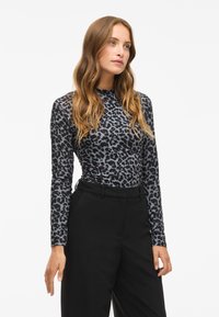 Long-sleeve top in gray with a black leopard print pattern, made of smooth fabric, paired with high-waisted black trousers.