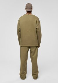 Khaki trainingspak bestaande uit een losse, geribbelde trui en bijpassende tapse broek. Beide stukken hebben een zachte textuur en minimale detailing.
