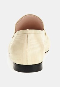 Beżowe satynowe buty wsuwane z niską czarną podeszwą. Posiadają gładką fakturę i zaokrąglony kształt. Widok z tyłu podkreśla detale przeszyć.