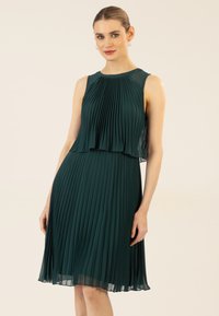 Grünes plissiertes Kleid mit ärmellosem Design, geschichteter Brustpartie und fließendem Rock. Leichter Stoff mit transparenter Überlagerung oben.