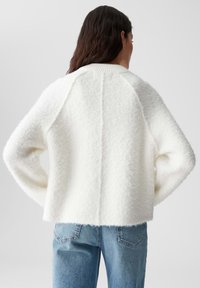 Witte, pluizige trui met een geribbelde kraag, raglanmouwen en een cropped pasvorm. Gekocht met blauwe denim jeans. Achteraanzicht, eenvoudig ontwerp.
