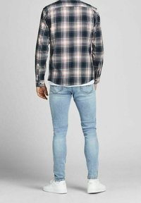 Karierter Button-Up-Hemd in Marineblau, Rot und Weiß; getragen über einem weißen T-Shirt. Slim-Fit hellblaue Jeans und weiße Sneakers. Ansicht von hinten.