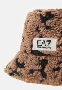 Brun, fluffy bøttehat med et sort abstrakt mønster. Har et mærket hvidt tag med "EA7 EMPORIO ARMANI" i sort skrift.
