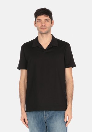 Polo shirt nero a maniche corte con una texture morbida e colletto a punta, indossato con jeans di denim azzurro chiaro. Design semplice e minimalista.