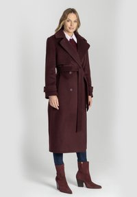 Bordowy wełniany płaszcz z podwójnym zapięciem, szerokim kołnierzem, regulowanym paskiem i mankietami zapinanymi na guziki, zestawiony z wysokimi do kostek, spiczastymi botkami.