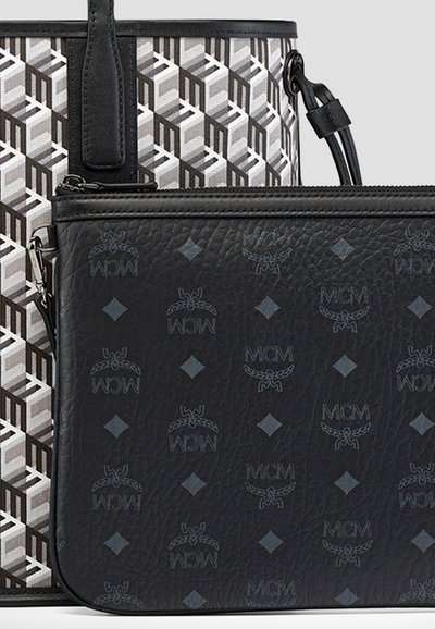 Schwarze Lederumschlagtasche mit MCM-Logos und einer grau-musterierten Tragetasche mit schwarzen Griffen dahinter.