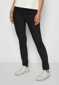 Zwarte broeken met een slim fit, voorzien van voorzakken met rits en een gladde textuur, gecombineerd met witte sneakers.
