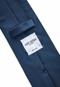 Mörkblå randig slips i strukturerat tyg, med en rektangulär vit etikett med svart text som anger "JOHN HENRIC SWEDEN" och "Tillverkad i Italien."