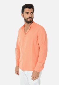 Camicia di lino arancione con colletto stand, maniche lunghe e chiusura con bottoni, caratterizzata da un tessuto testurizzato e una vestibilità rilassata.